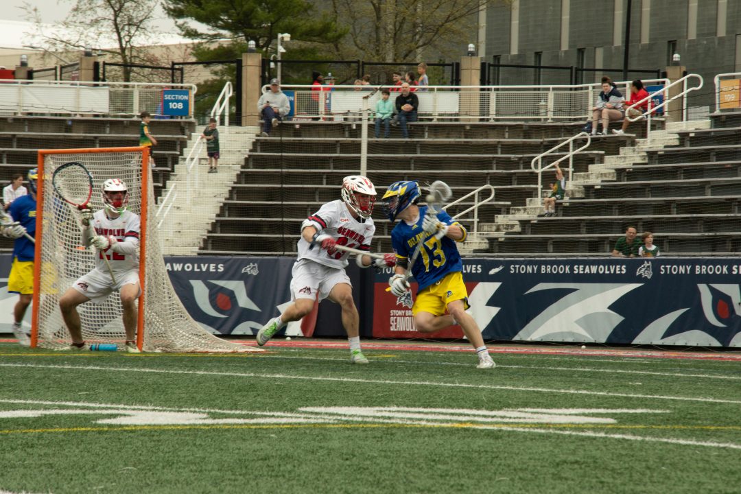 Defender Dan Newton (99) face guards Delaware midfielder Brendan Powers on Saturday, April 15 while goalkeeper Jamison MacLachlan (22) prepares for a save attempt. The third-seeded Stony Brook mens lacrosse team lost in the CAA championship game to the top-seeded Delaware Blue Hens on Saturday. TIM GIORLANDO/THE STATESMAN